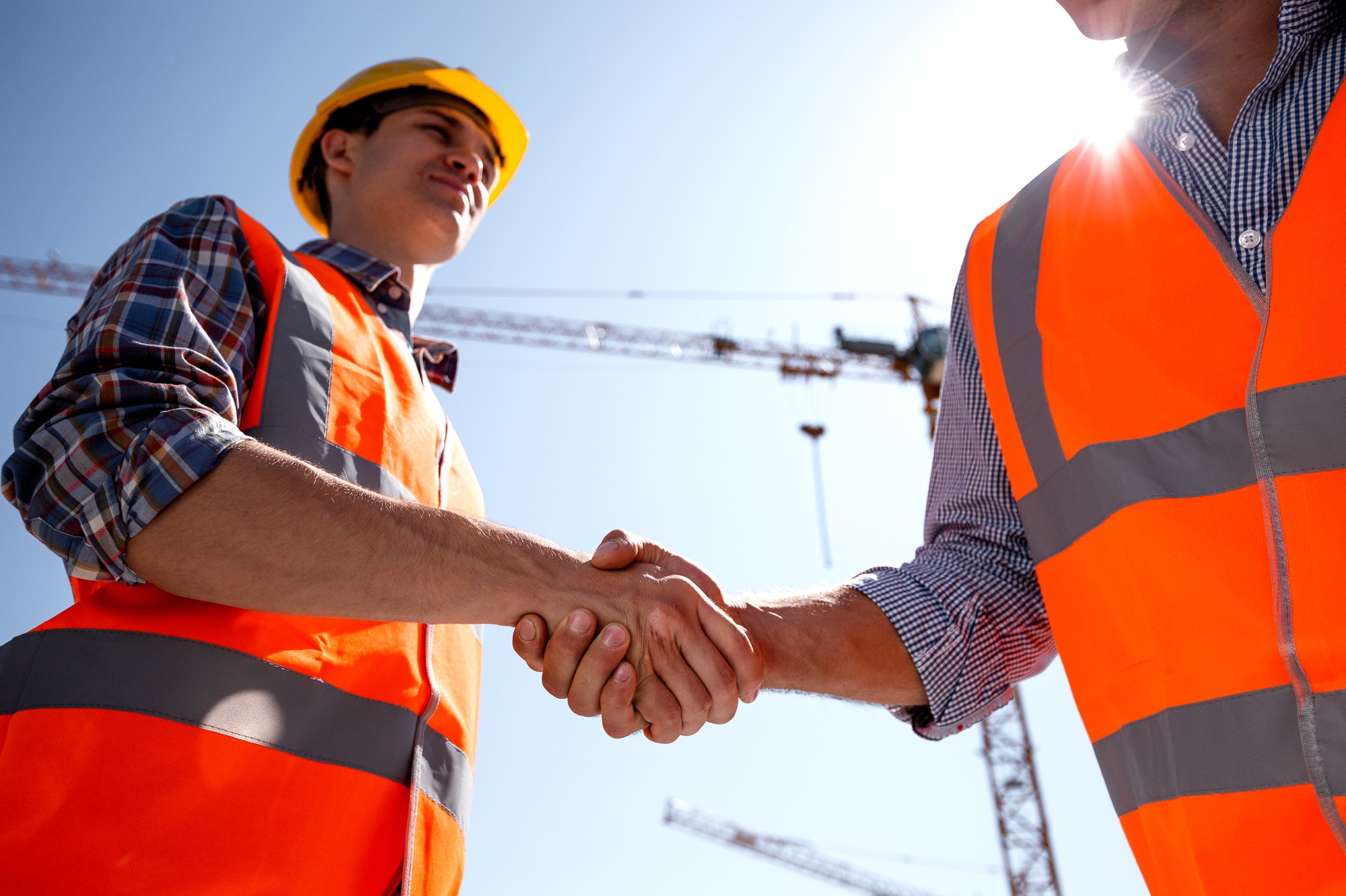 Structural engineer and architect dressed in orange work vests and helmets shake hands on the.jpg
